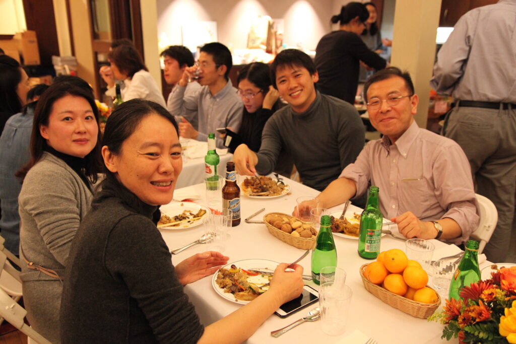 Prof. Chikamoto and three other scholars smile at the camera. They are seated with food and drink in front of them.