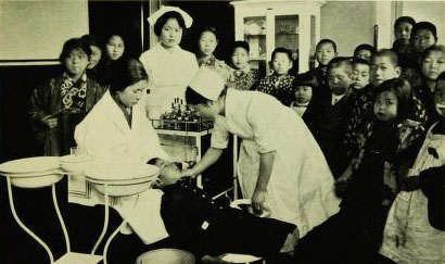 Several young students attend an eye clinic; nurses examine one student's face