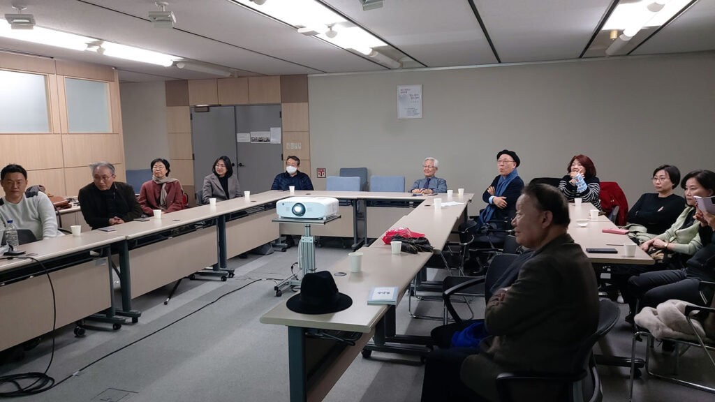 Audience members sit around a U-shaped table listening to a presentation