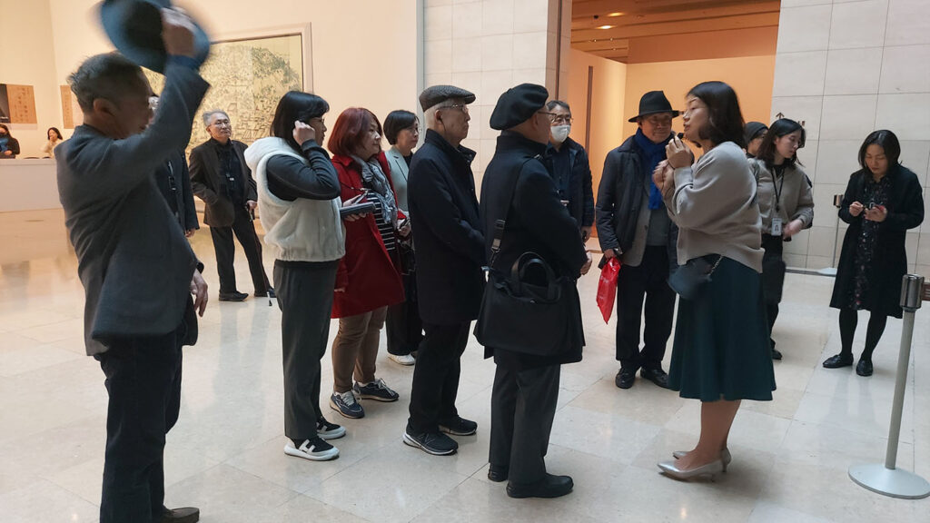 A dozen alumni listen to a guided tour of a museum exhibit